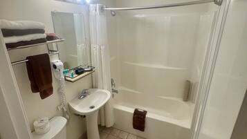 Un baño con inodoro, lavamanos y bañera. Hay un perchero con toallas, un espejo y una cortina de ducha.