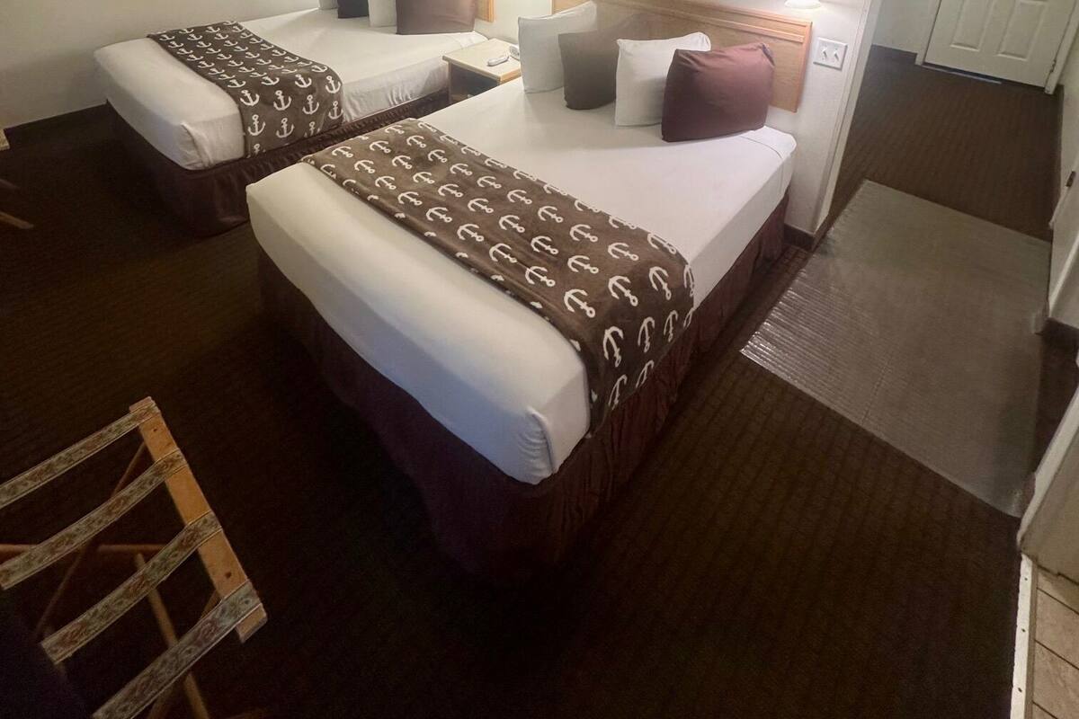 A hotel room with two beds, a small table, a chair, and a door leading to a hallway.