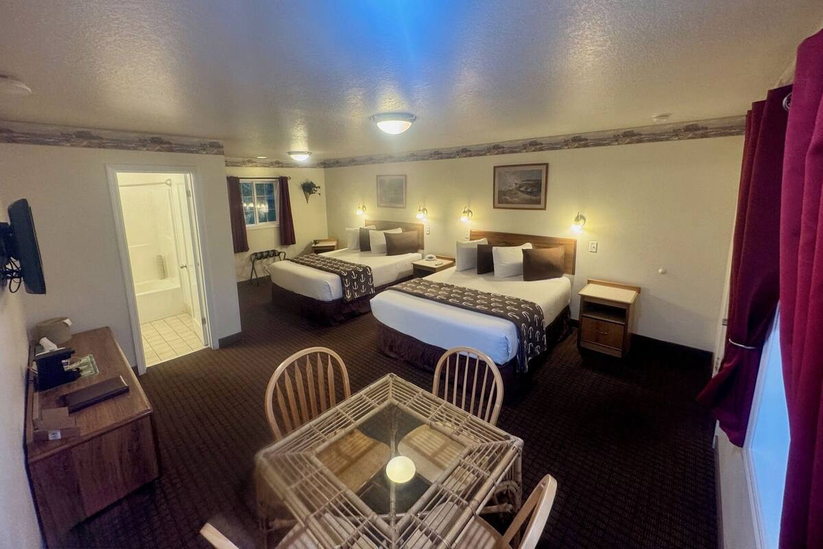 A hotel room with two beds, a dining table, and a small desk.