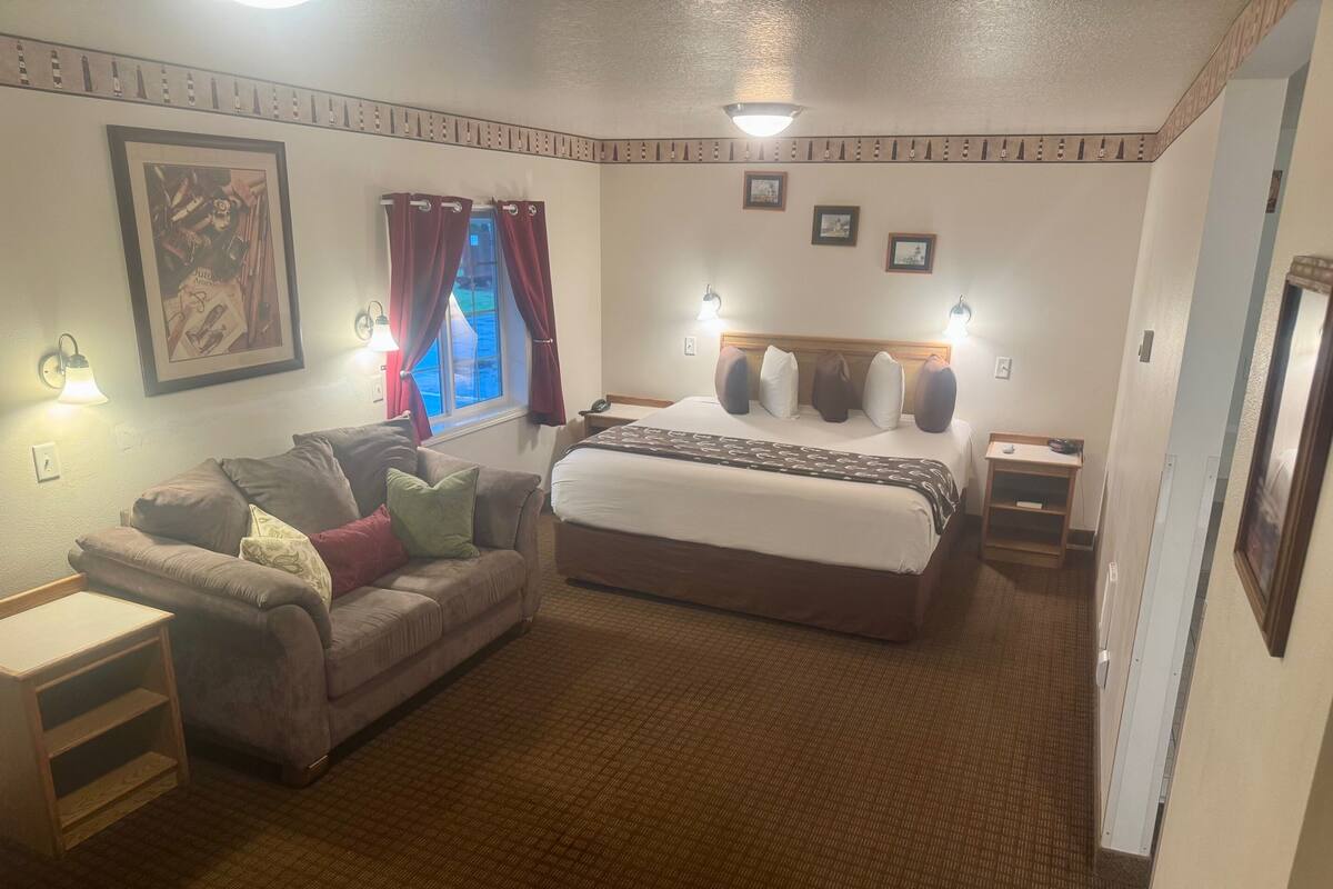 A hotel room with a bed, a sofa, a nightstand, and a lamp.
