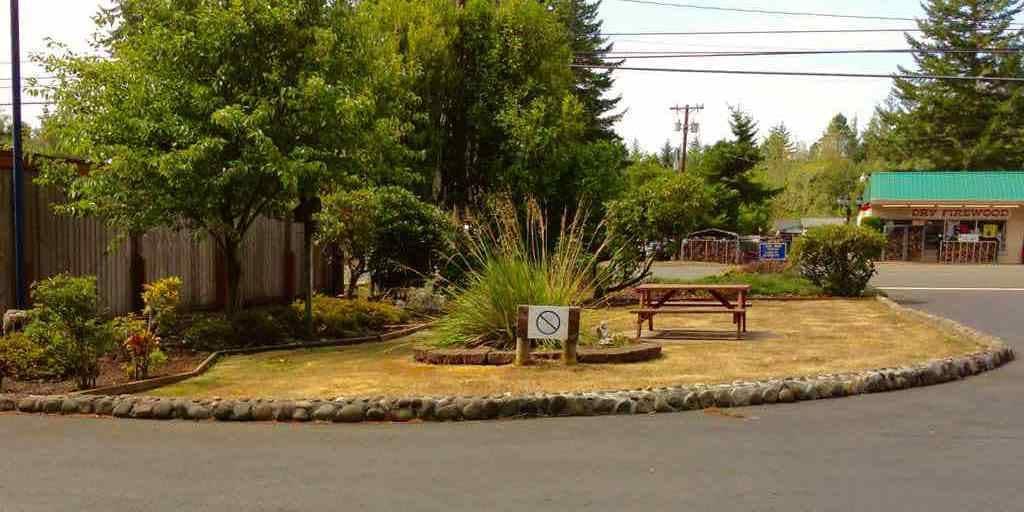 Uma área de descanso à beira da estrada, com uma mesa de piquenique, placa de proibição de estacionamento e um pequeno edifício ao fundo.