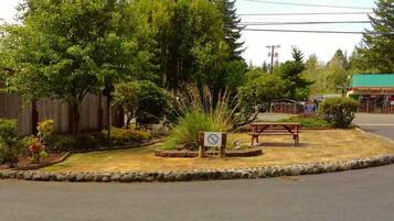Uma área de descanso à beira da estrada, com uma mesa de piquenique, placa de proibição de estacionamento e um pequeno edifício ao fundo.