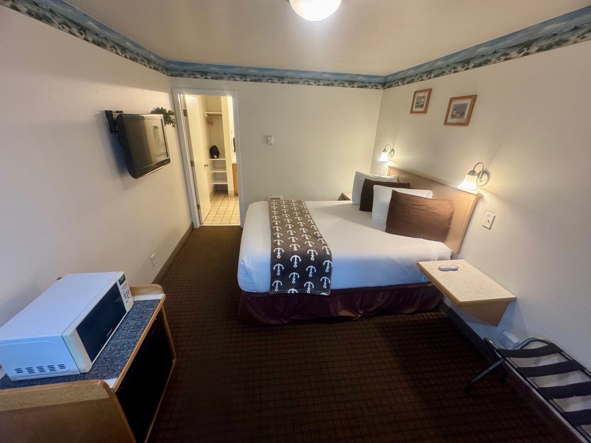 A hotel room with a bed, bedside tables, a TV, a microwave, and a door leading to a hallway.