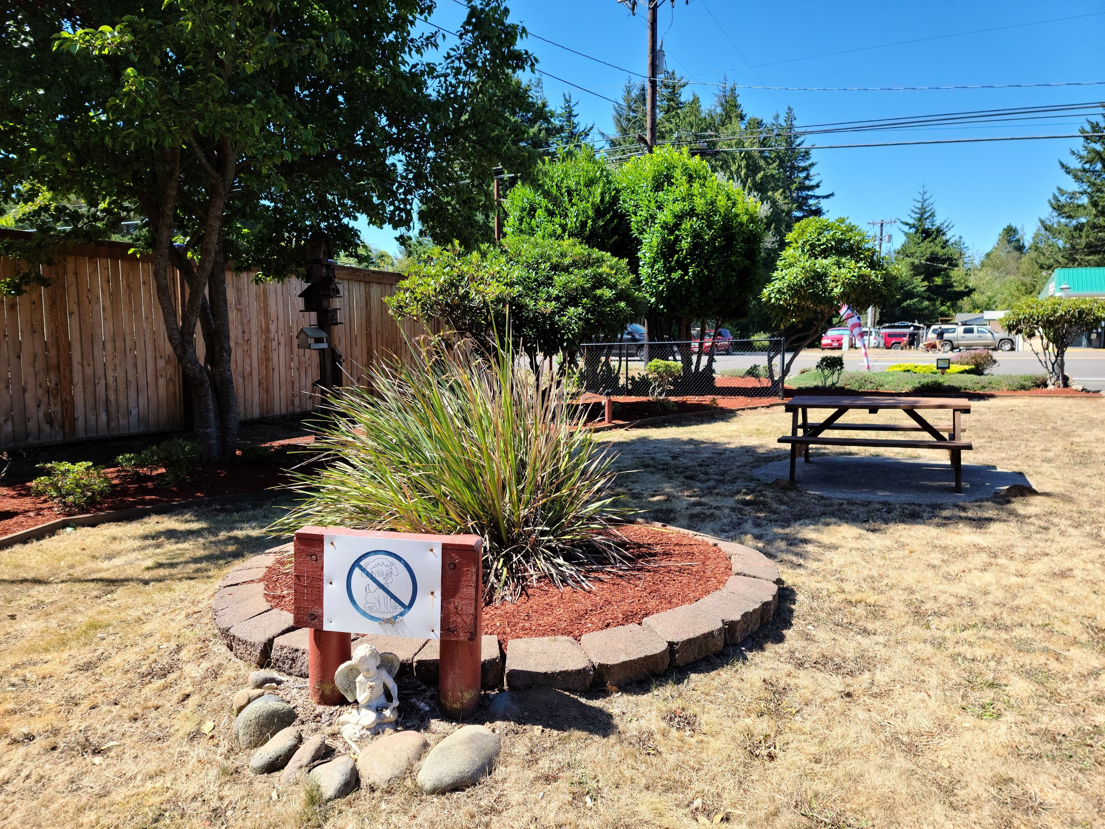 Área de jardim cercada com mesa de piquenique, placa de proibido e estátua de anjo.