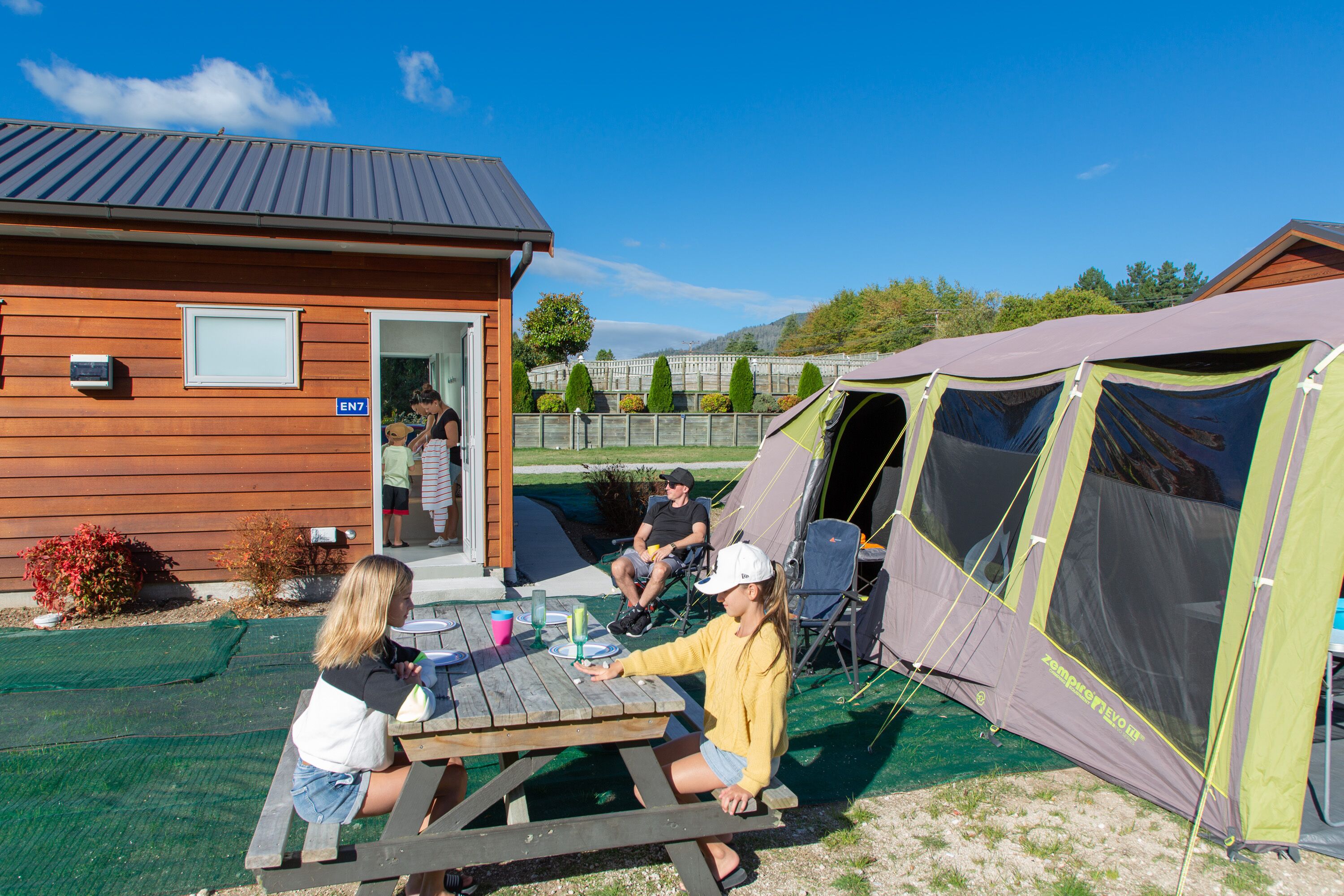 A wooden building with a door, a picnic table, and a tent.