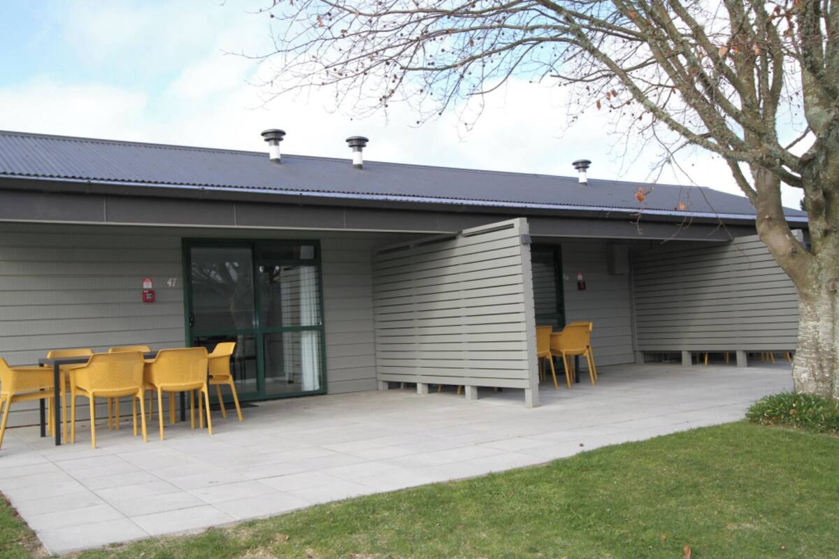 Een gebouw met een overdekte patio, buiten zitplaatsen en een boom.