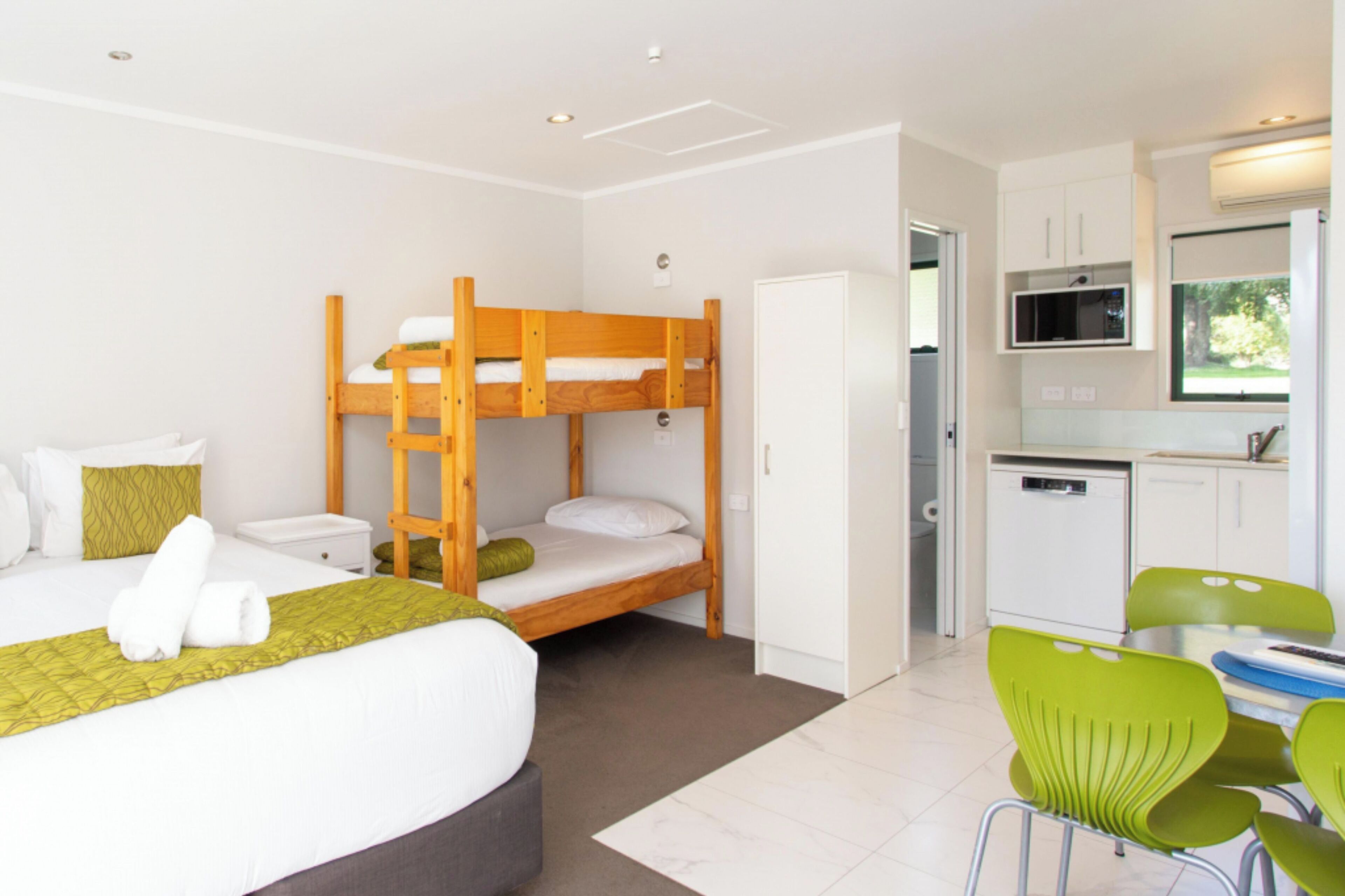 A room with bunk beds, a small kitchenette, and a dining area with green chairs.