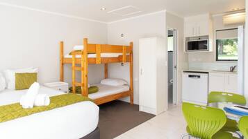 A room with bunk beds, a small kitchenette, and a dining area with green chairs.