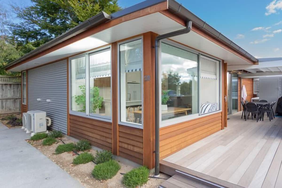 Een modern, gelijkvloers huis met grote ramen, een houten terras en een overdekte zithoek buiten.