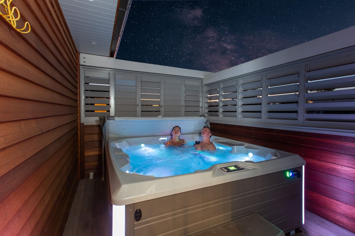 A hot tub with two people, wooden deck, and a starry night sky.