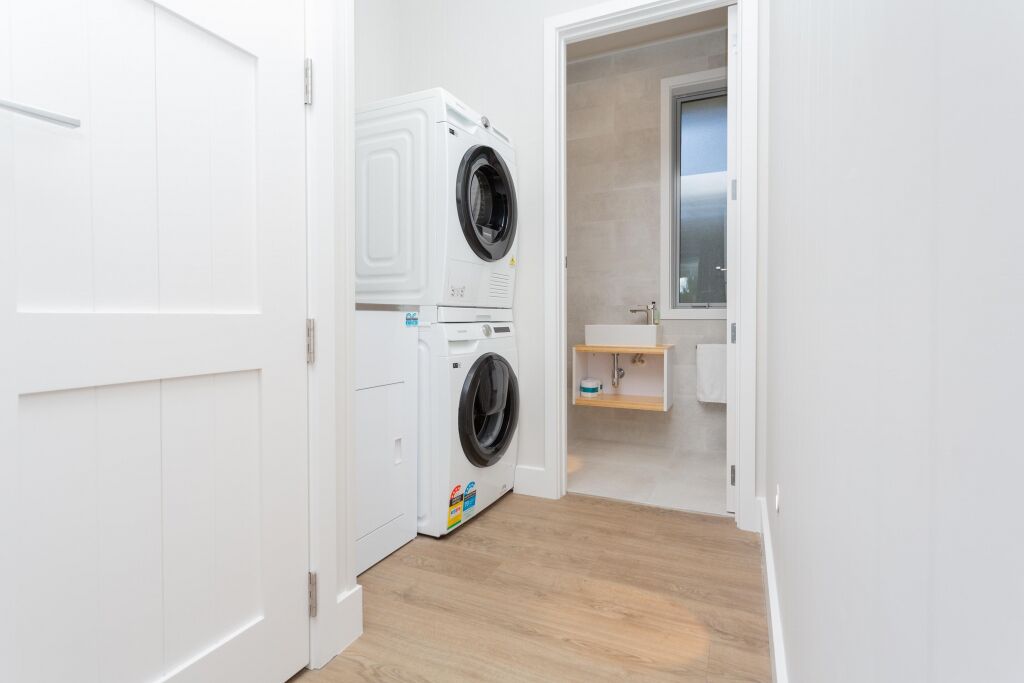 A laundry room with stacked washers and dryers, a wooden floor, and a small window.