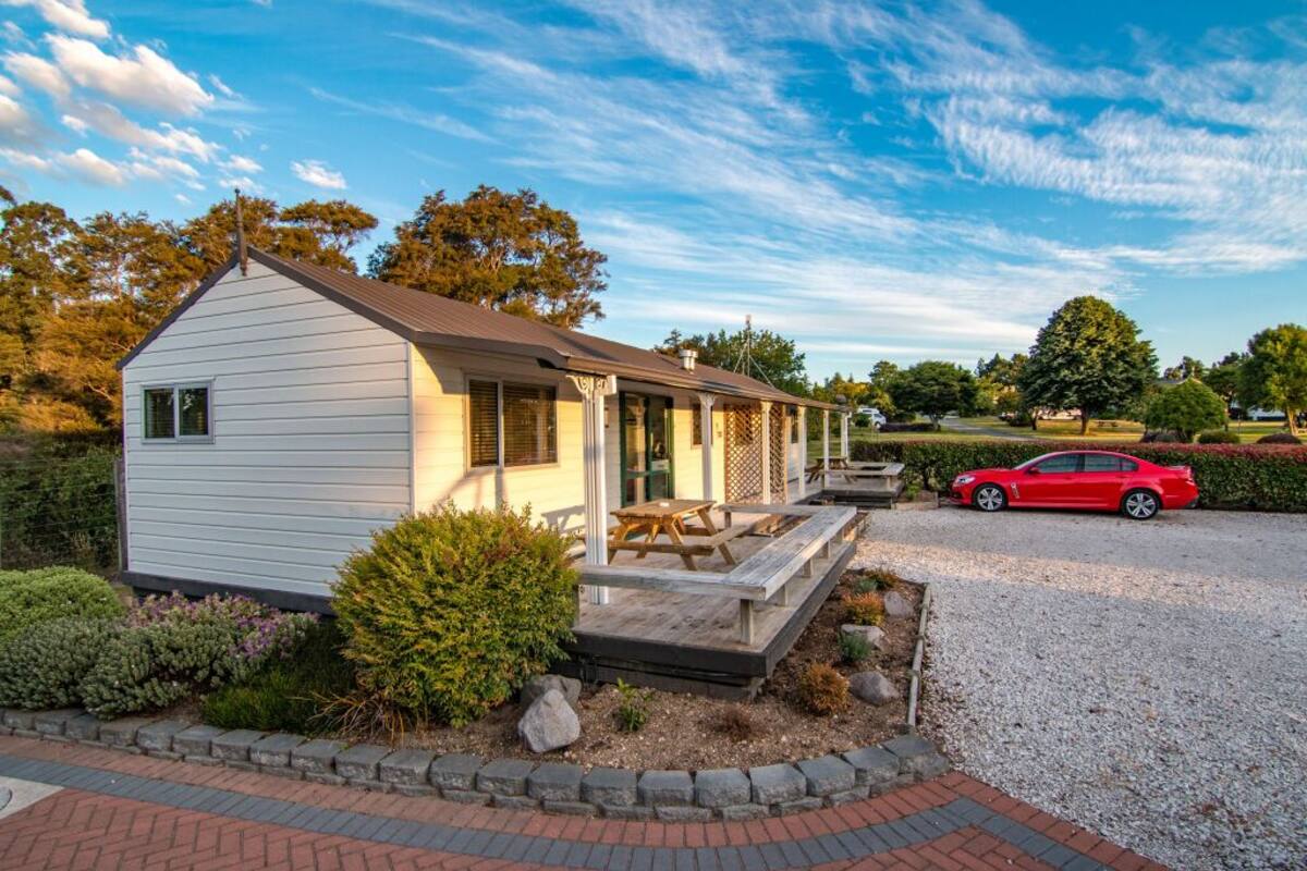 Een gelijkvloers huis met een veranda, een grindpad en een rode auto op de achtergrond.