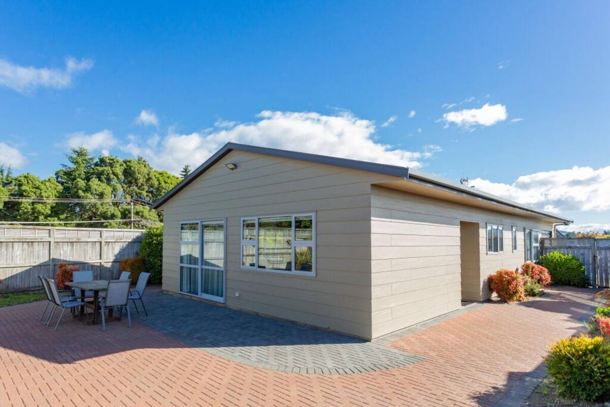 Een gelijkvloers huis met een terras, een tafeltje met stoelen, en een houten hek op de achtergrond.