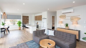 Un salon moderne avec un canapé d’angle gris, une table basse en bois et un coin repas comprenant une table et des chaises blanches.