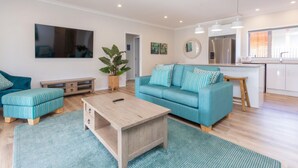 Un salon moderne avec un canapé de couleur turquoise, une table basse en bois et un pouf à rayures.
