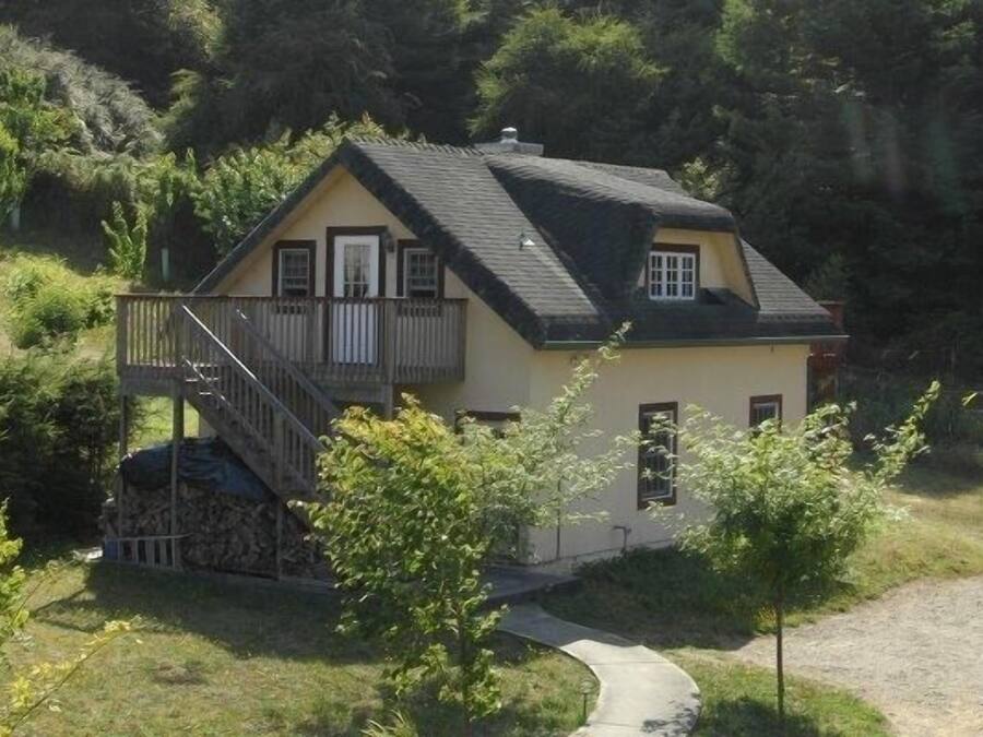 Uma casa térrea com varanda, rodeada por vegetação e um caminho que leva à entrada.