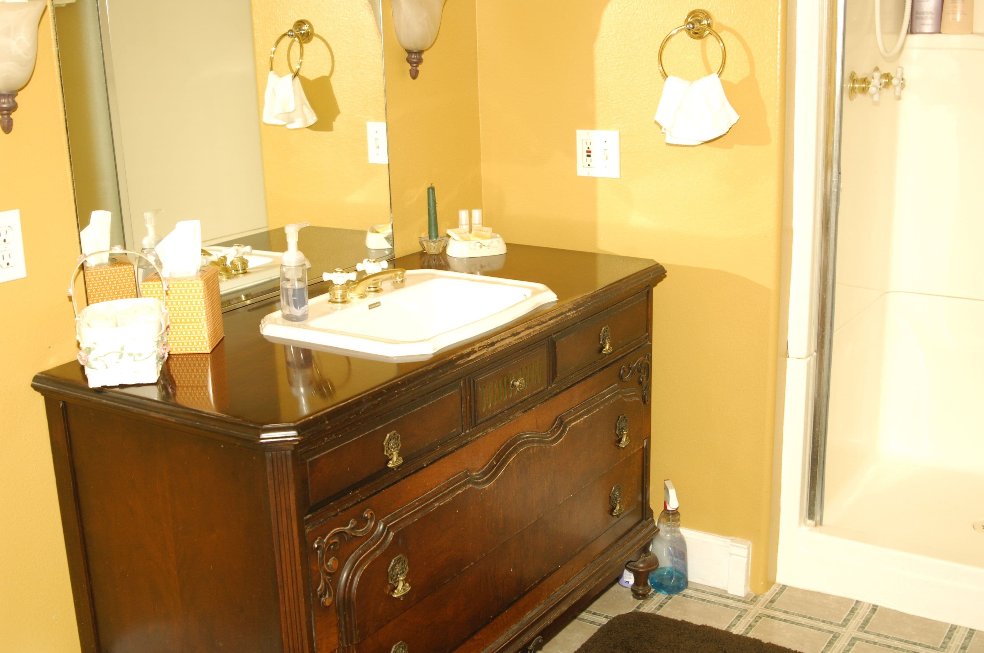 A bathroom with a wooden vanity, a mirror, a sink, and a shower.