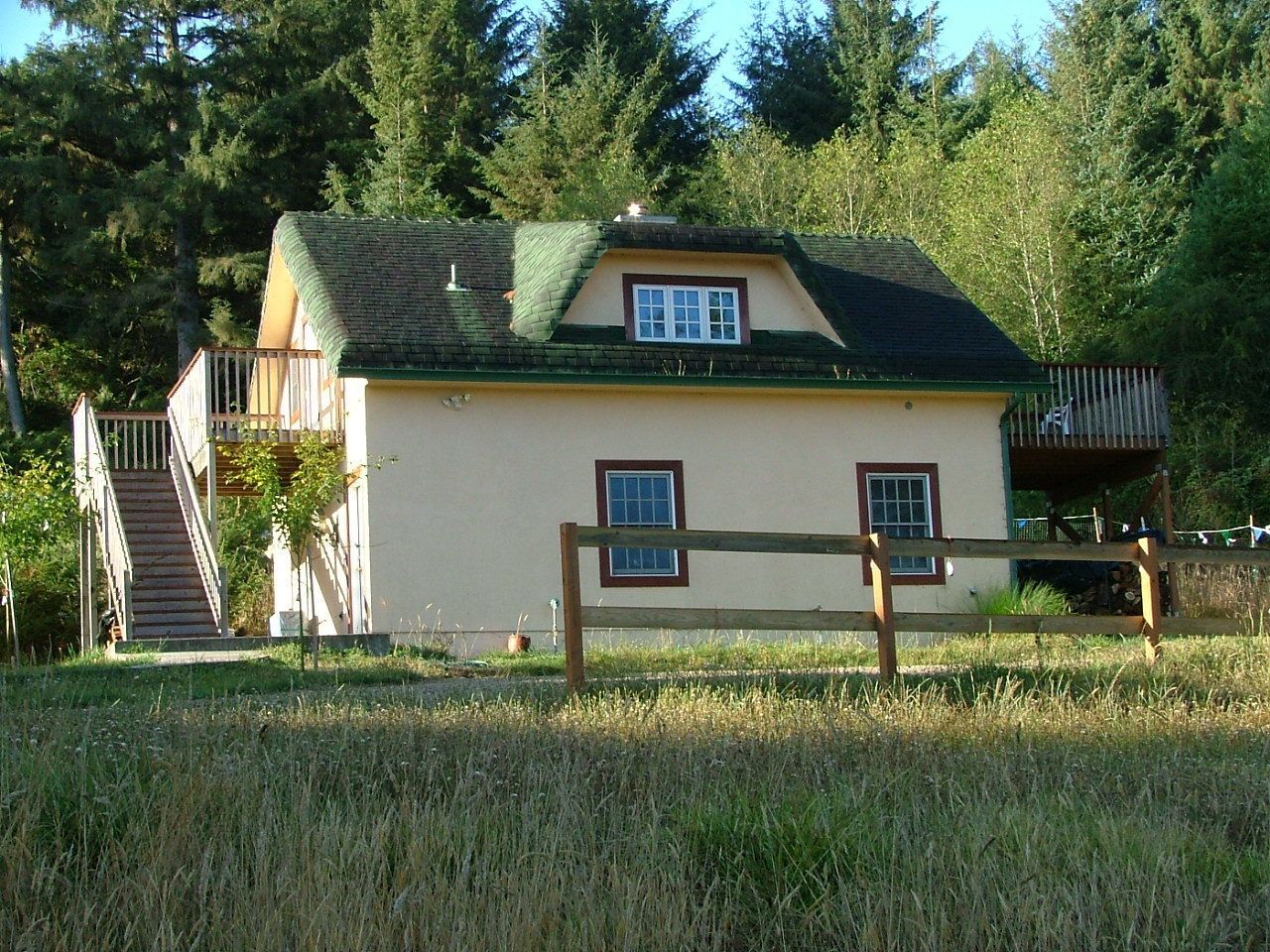 Ein zweistöckiges Haus mit grüner Dachbegrünung, einer kleinen Veranda und einem Holzzaun davor.