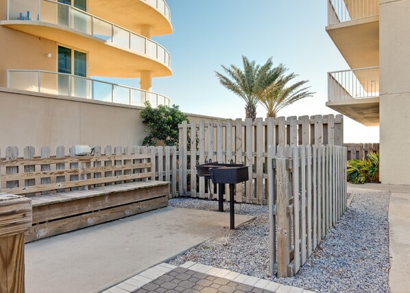 A courtyard with a wooden bench, a barbecue grill, and a palm tree.