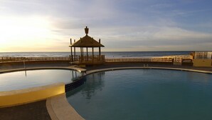 A large, curved pool with a gazebo structure in the center, surrounded by a wooden deck and a low wall. - Summer House on Romar Beach by Wyndham Vacation Rentals (Orange Beach)