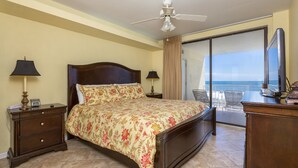 A hotel room with a bed, a ceiling fan, a nightstand, a desk, a chair, and a view of the ocean. - Summer House on Romar Beach by Wyndham Vacation Rentals (Orange Beach)