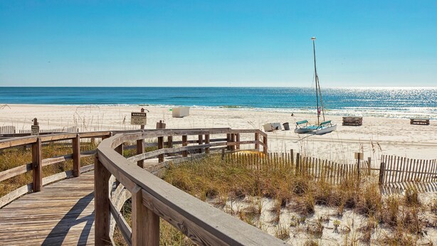A wooden boardwalk leading to a sandy beach with a clear blue sky. - Summer House on Romar Beach by Wyndham Vacation Rentals (Orange Beach)