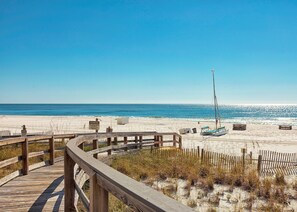 A wooden boardwalk leading to a sandy beach with a clear blue sky.
