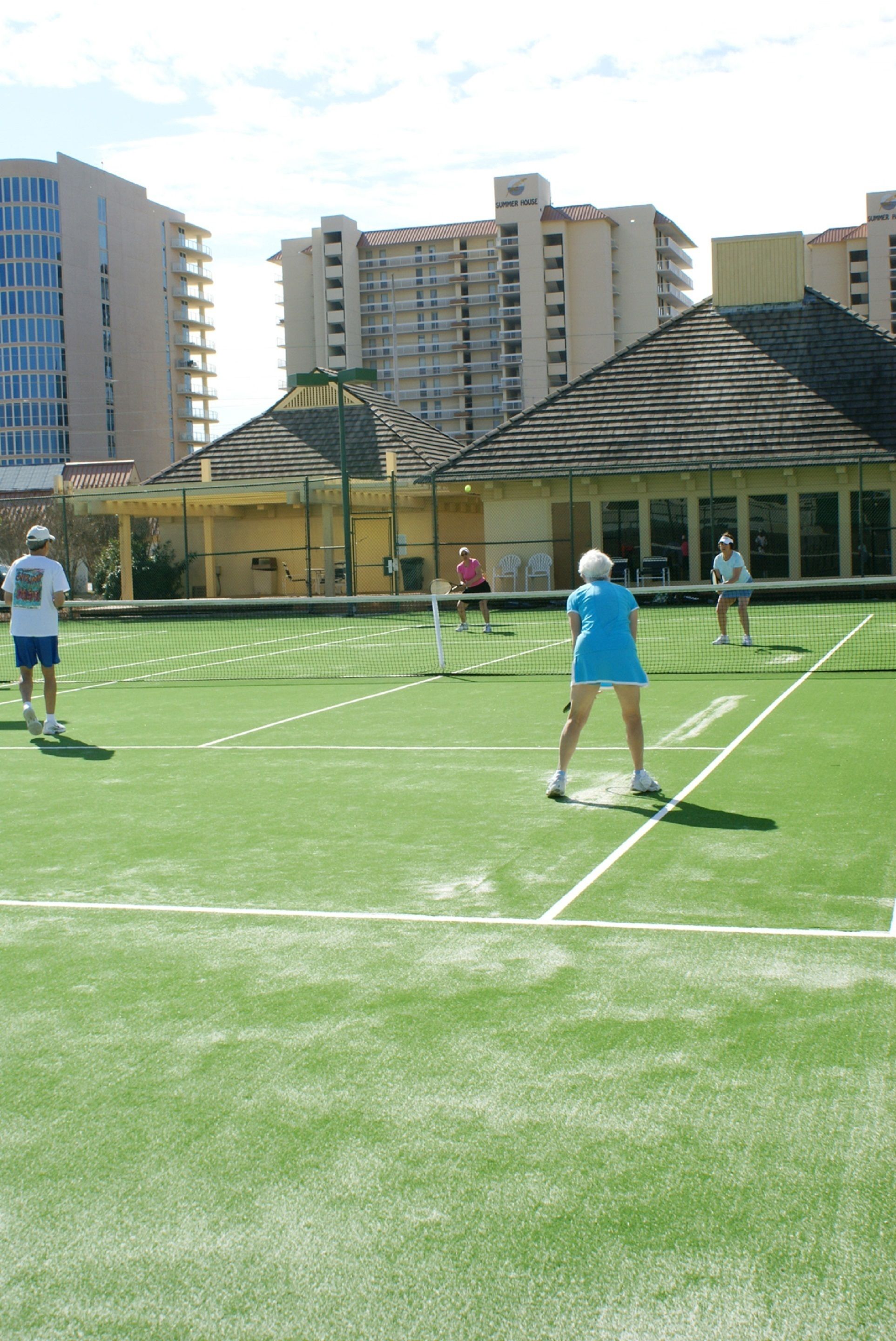 Een tennisbaan met spelers, omringd door gebouwen.