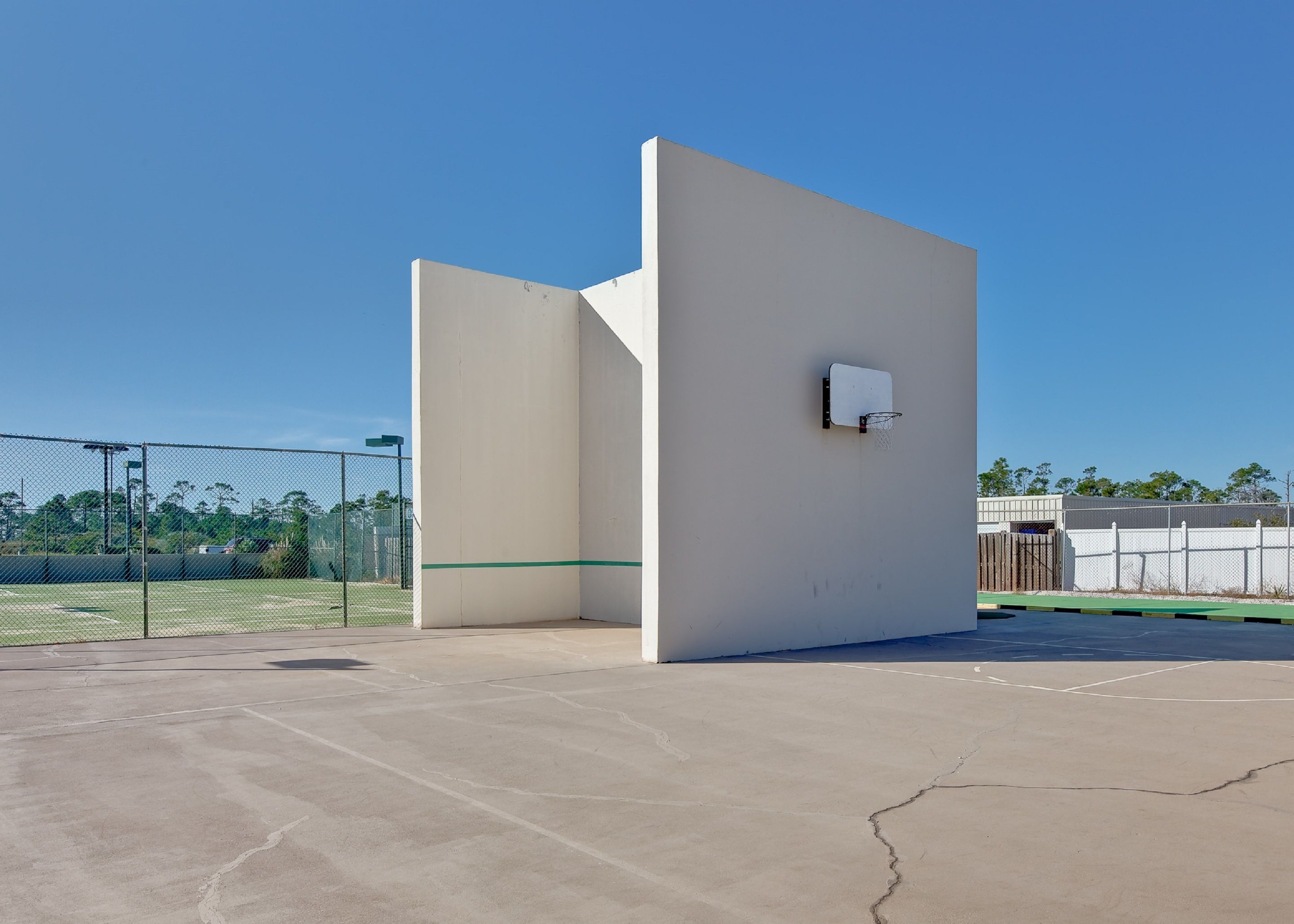 A basketball court with a chain-link fence, a basketball hoop, and a concrete surface.
