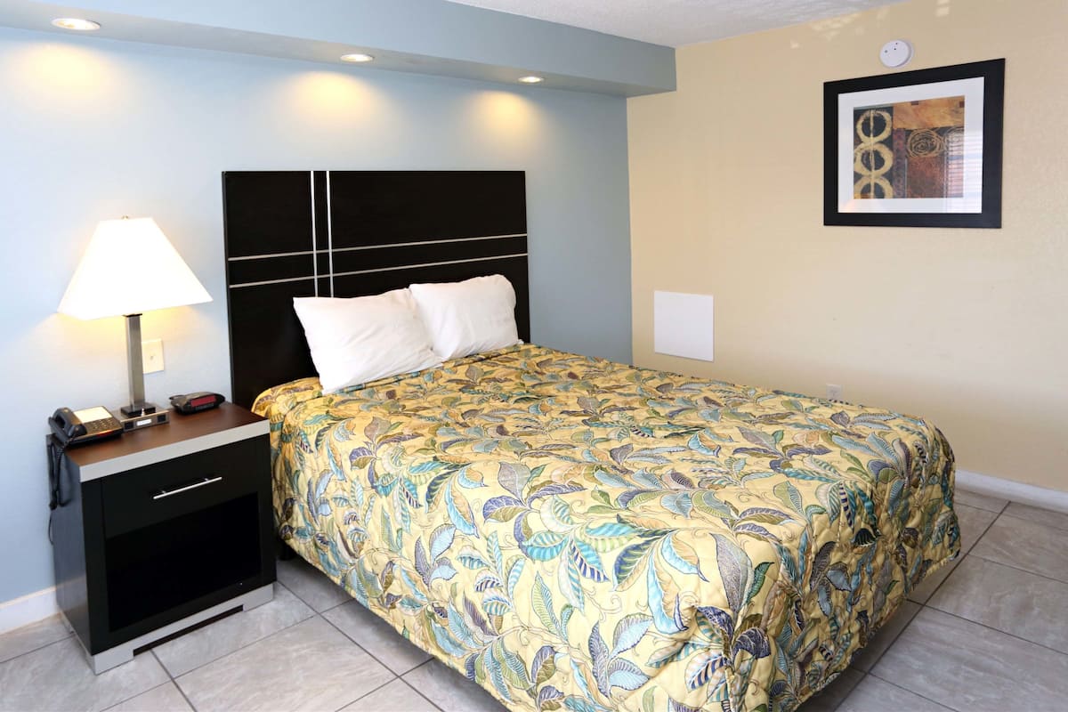 A hotel room with a bed, bedside table, lamp, and a framed picture on the wall.