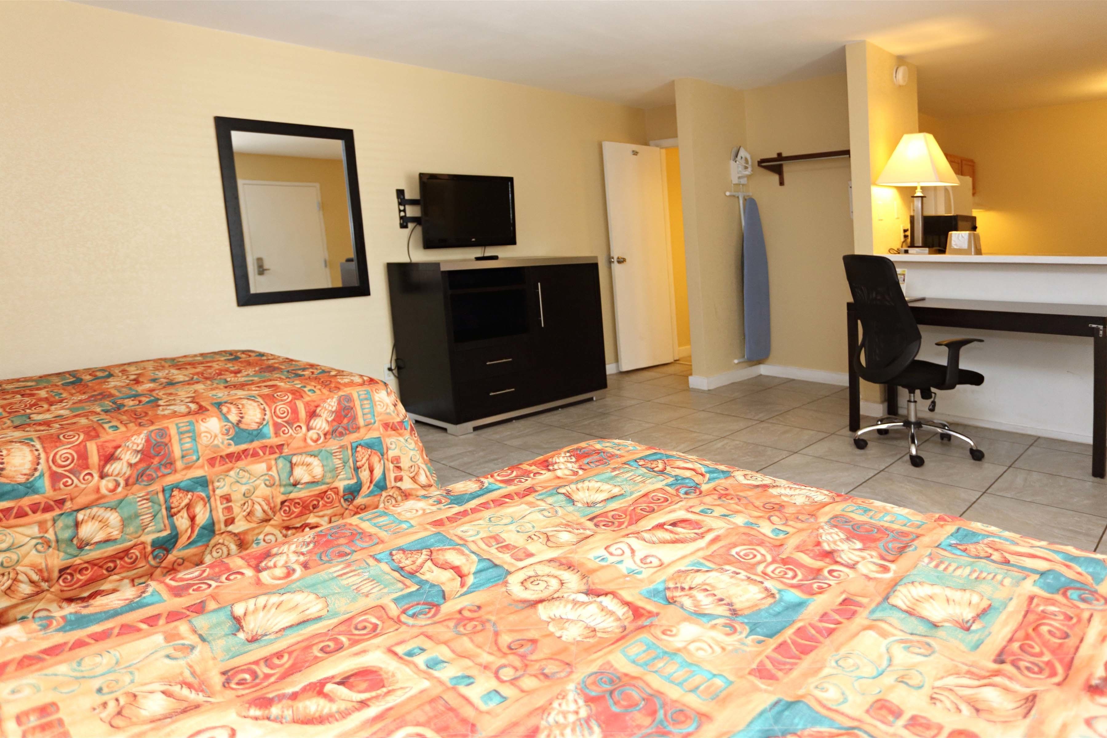 A hotel room with two beds, a desk, a chair, a television, and a mirror.