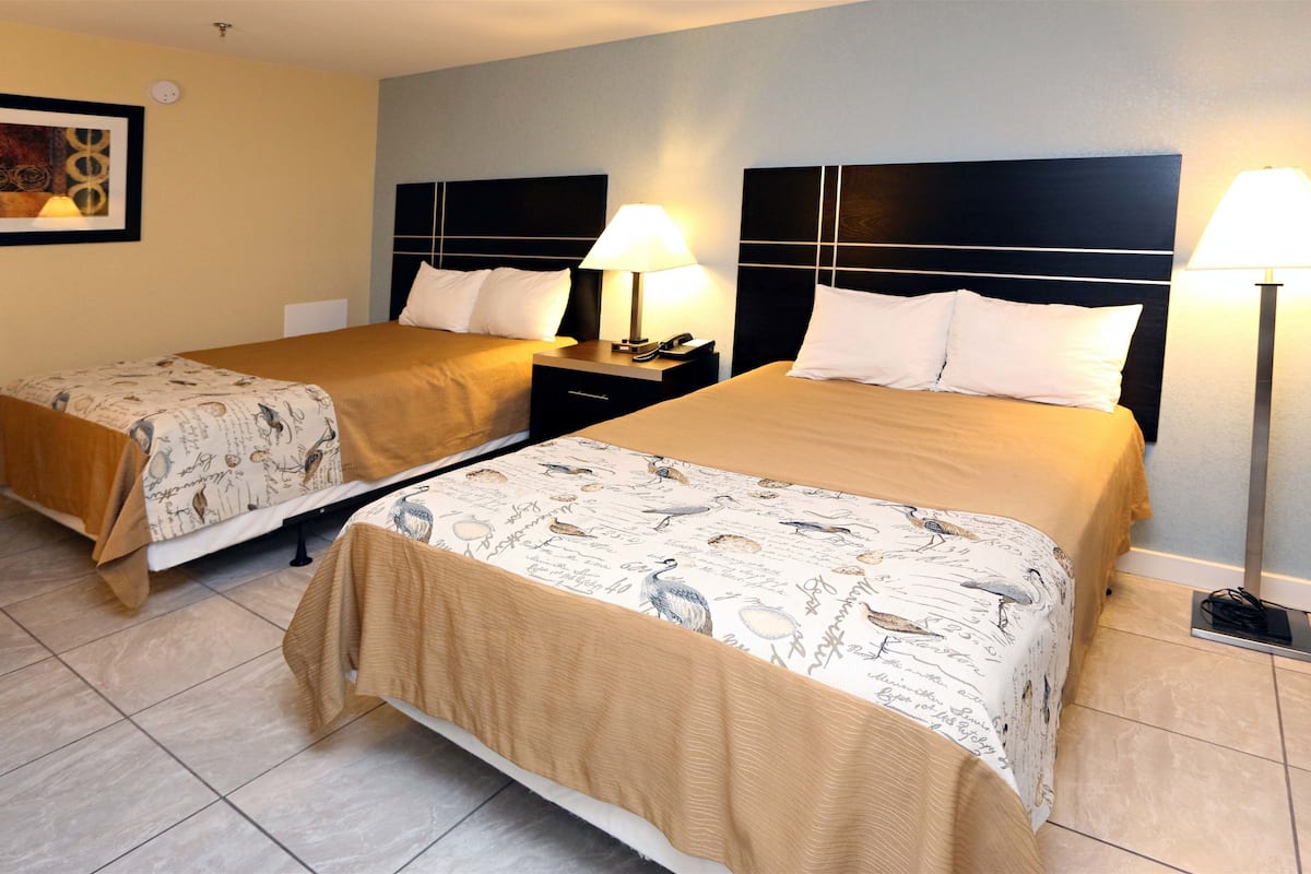 A hotel room with two beds, each with a headboard, bedside tables, lamps, and a wall-mounted artwork.