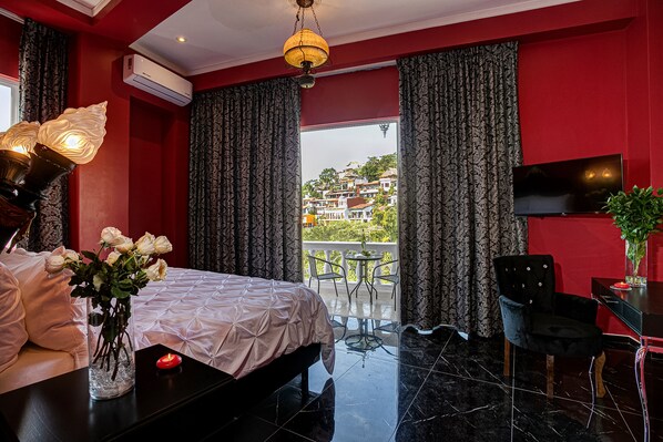 A hotel room with a bed, a bedside table with a vase of flowers, a TV, a chair, and a balcony with a view of buildings.