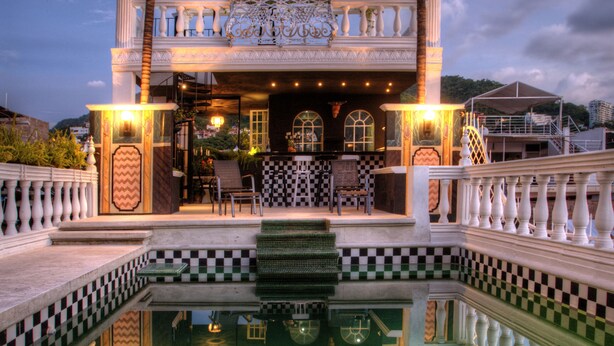 A pool with a checkered pattern, palm trees, and a balcony with chairs and tables. - Rivera del Rio Boutique Hotel (Puerto Vallarta)