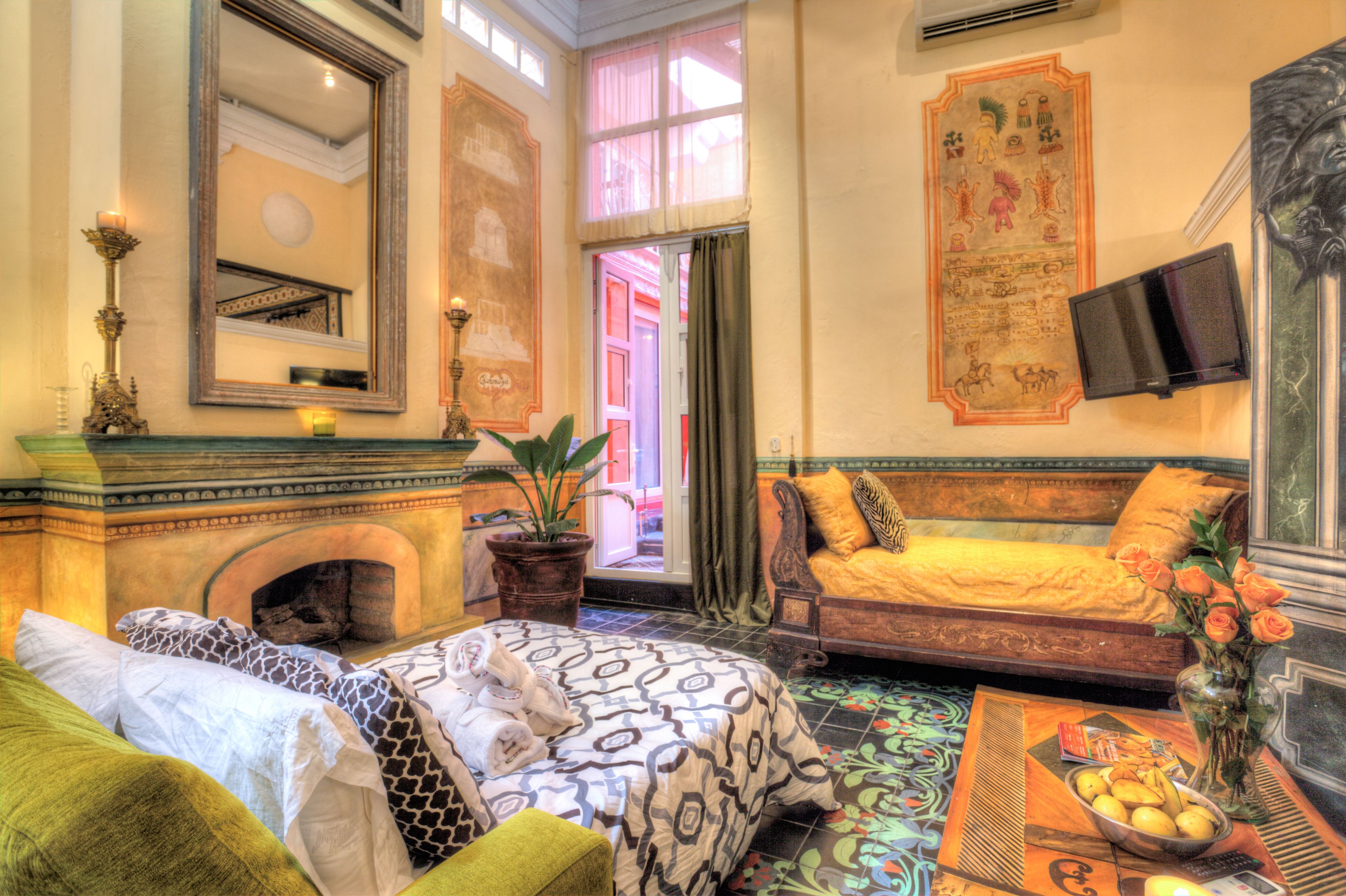Ein Zimmer mit Kamin, einem Bett mit gemusterten Textilien, einer Couch mit Kissen, einem Tisch mit Blumenvase und einem Wand-Fernseher.
