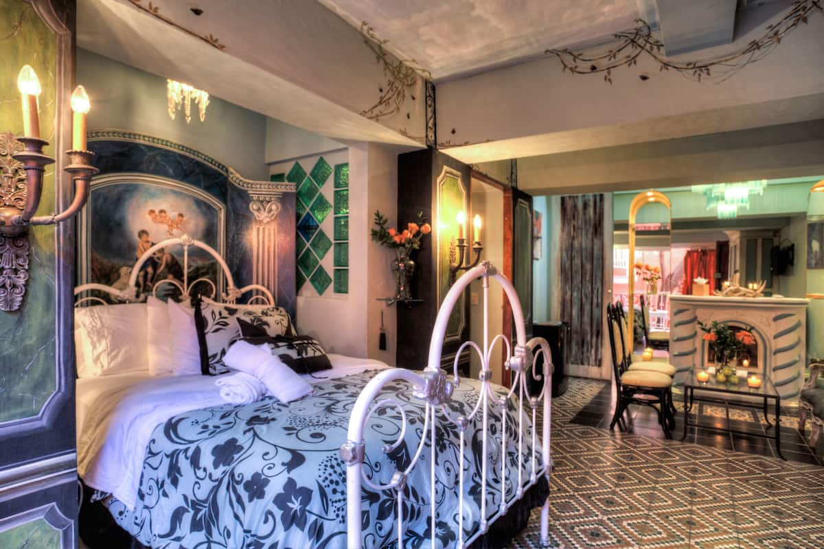 A bedroom with a bed, a chair, a table, and a mirror.