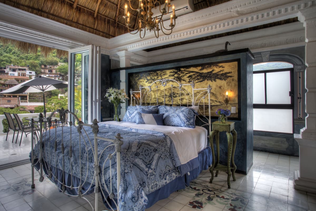 A bedroom with a large bed, a chandelier, and a view of the outside.