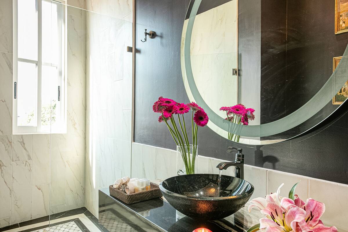 A modern bathroom with a black sink, a large mirror, and a vase of pink flowers.