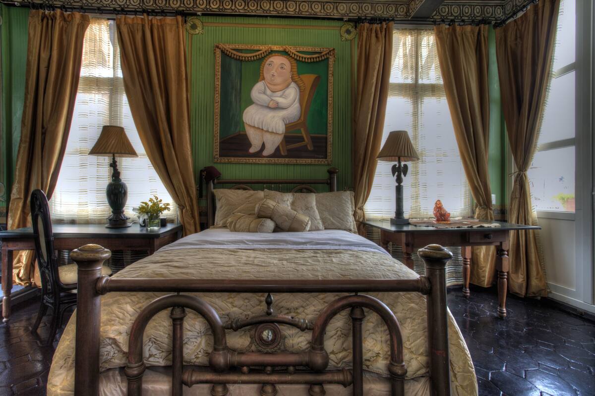 A bedroom with a large bed, two nightstands, a chair, and a painting on the wall.