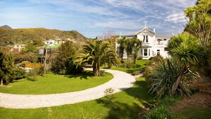 A large white building with a symmetrical facade, surrounded by lush greenery and a winding gravel path. - Sennen House (Picton)