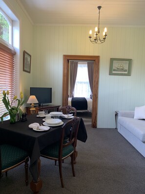 Un coin repas avec une table dressée pour quatre personnes, un téléviseur et une vue sur une chambre à coucher avec un lit et des rideaux.