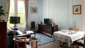 A room with a dining table set for four, a television, a cabinet, a sofa, and a chair. - Sennen House (Picton)