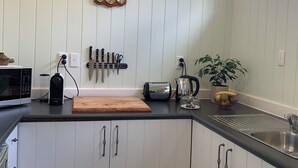 A kitchen with white cabinets, a wooden countertop, a microwave, a toaster, and a kettle. - Sennen House (Picton)