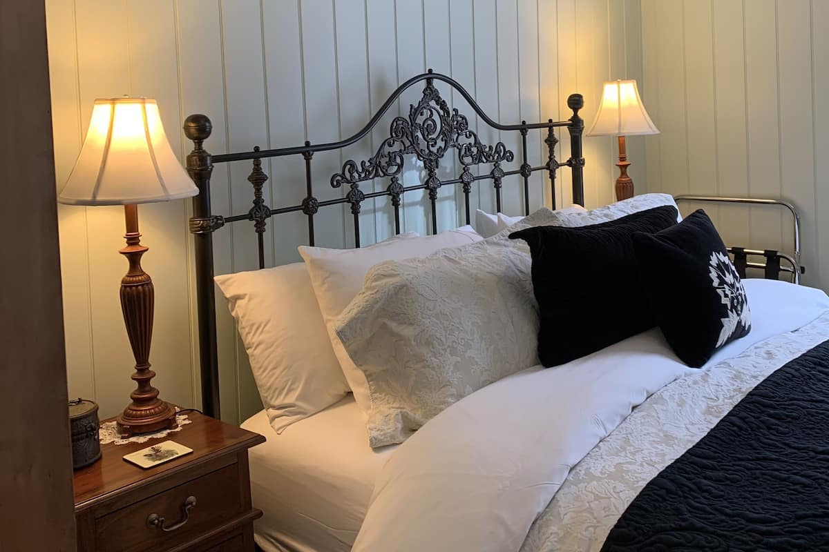 A neatly made bed with white and black bedding, two bedside lamps, a wooden nightstand, and a framed picture on the wall.