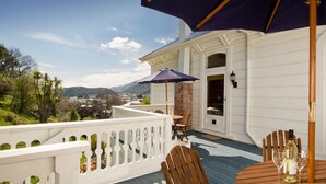 A wooden deck with a table and chairs, a bottle of wine, and a blue umbrella. - Sennen House (Picton)