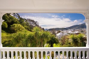 Un balcon doté d’une balustrade blanche, qui offre une vue sur un jardin luxuriant et sur une ville située au loin.
