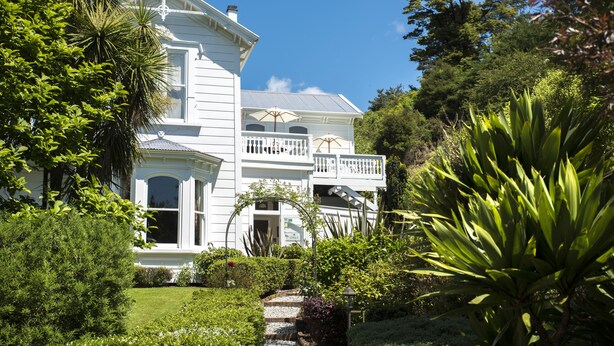 A large white two-story house with a balcony, surrounded by lush greenery and a well-maintained garden. - Sennen House (Picton)