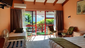 Une chambre d’hôtel avec deux lits, un bureau, une chaise, un ventilateur et une vue sur l’extérieur.