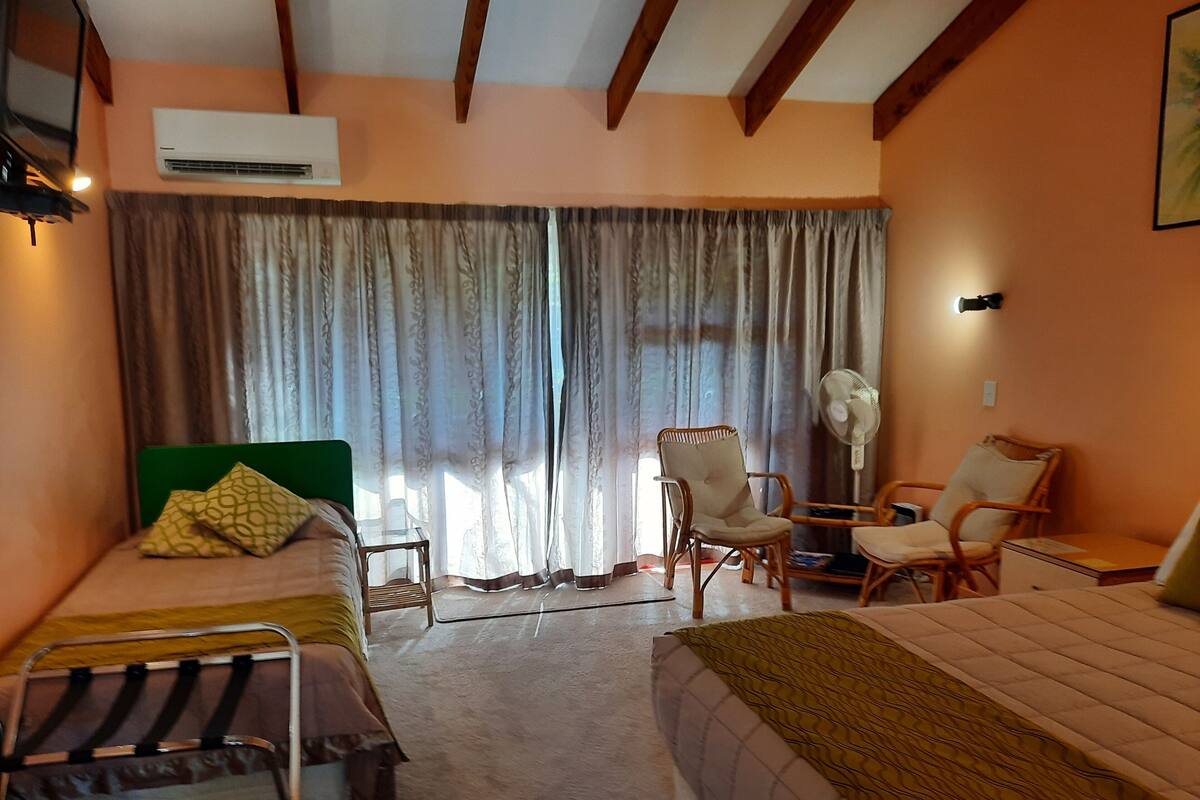 A hotel room with two single beds, a chair, a desk, and a large window with curtains.