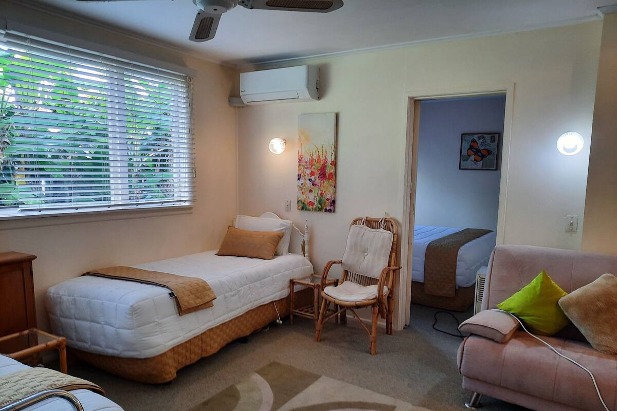 A bedroom with a bed, a chair, a sofa, and a window with blinds.